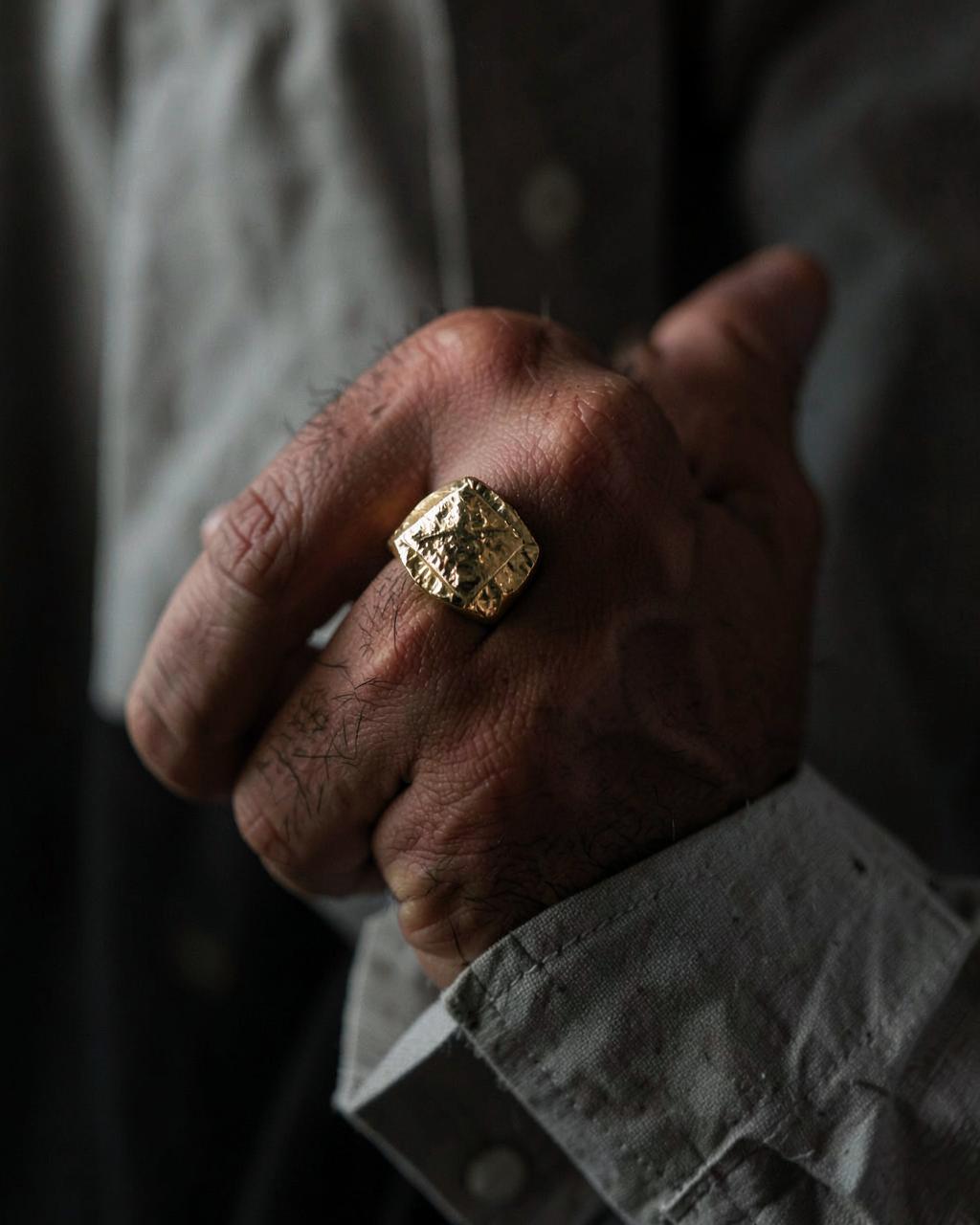 Man's hand wearing a heavy hand-hammered gold signet ring